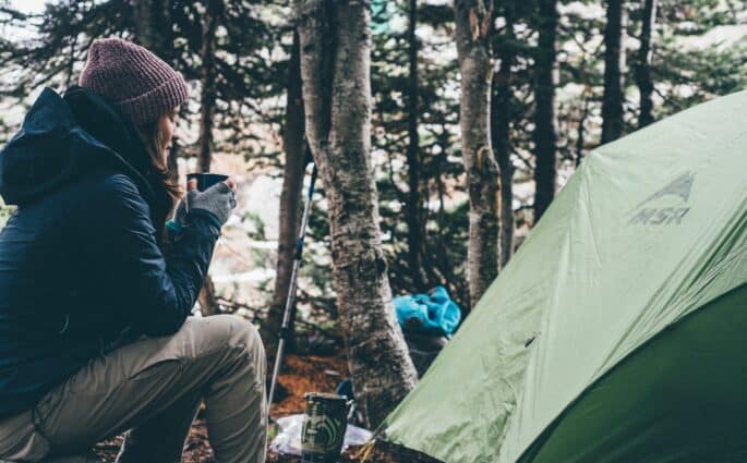 kobieta siedząca w lesie obok namiotu