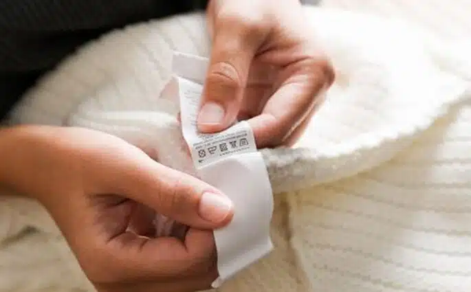 Kobieta trzyma w dłoni metkę i czyta znaki czyta oznaczenia